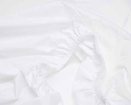Close up view of the elastic of a white hotel fitted bed sheet.